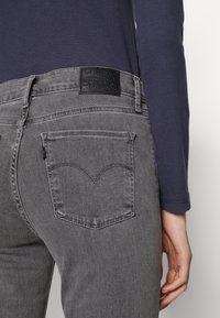 Grå denimjeans har en läderlapp på midjebandet, rundade bakfickor och en lätt sliten textur. Overdelen är marinblå.