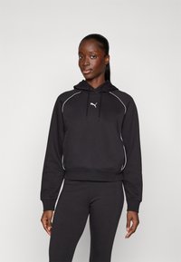Svart hettegenser med hvite piping-detaljer, med snøring i hetta og en liten logo på brystet, kombinert med matchende svarte leggings.