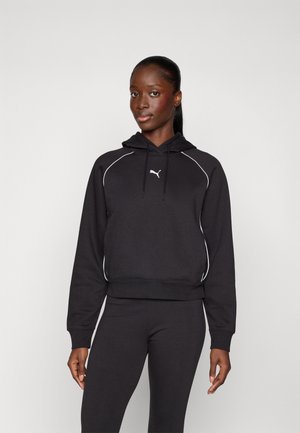 Svart hettegenser med hvite piping-detaljer, med snøring i hetta og en liten logo på brystet, kombinert med matchende svarte leggings.