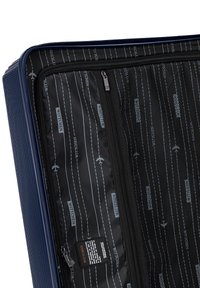 Valigia rigida di colore blu scuro con scanalature verticali. L'interno presenta una foderatura nera con motivi a tema viaggio in bianco, inclusi loghi e aerei.