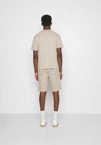 Beige tričko a šortky, bavlněný materiál, volný střih. Bílé tenisky s gumovou podrážkou a ponožky do kotníků. Jednoduchý design, bez vzorů.