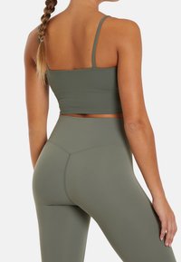 Top deportivo corto de color verde oliva con tirantes finos, combinado con leggings de cintura alta, que cuentan con un diseño sin costuras y una textura suave.