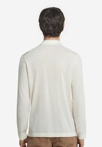 Långärmad skjorta i off-white, tillverkad av mjukt tyg. Har en kragkrage och en rak nederkant. Tyget verkar lätt och slätt.