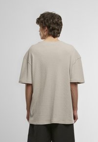 Tricou scurt cu mânecă scurtă, de culoare bej deschis, cu un material texturat, croială lejeră, gât rotund și umeri lăsați, având o tivă dreaptă.