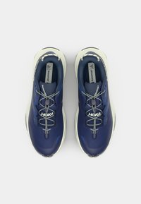 Baskets de sport bleues avec une tige texturée, une semelle intermédiaire blanche et des accents réfléchissants. Présente un logo et des lacets à motifs.