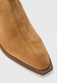 Suede ankelstøvlette i brunt med spids tå og en glat, tekstureret overflade. Accentueret med en brun sål og minimale syninger.