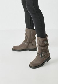 Botines de ante gris con cremalleras laterales, hebillas y acentos metálicos; suelas de goma gruesa; diseño arrugado; acabado texturizado.