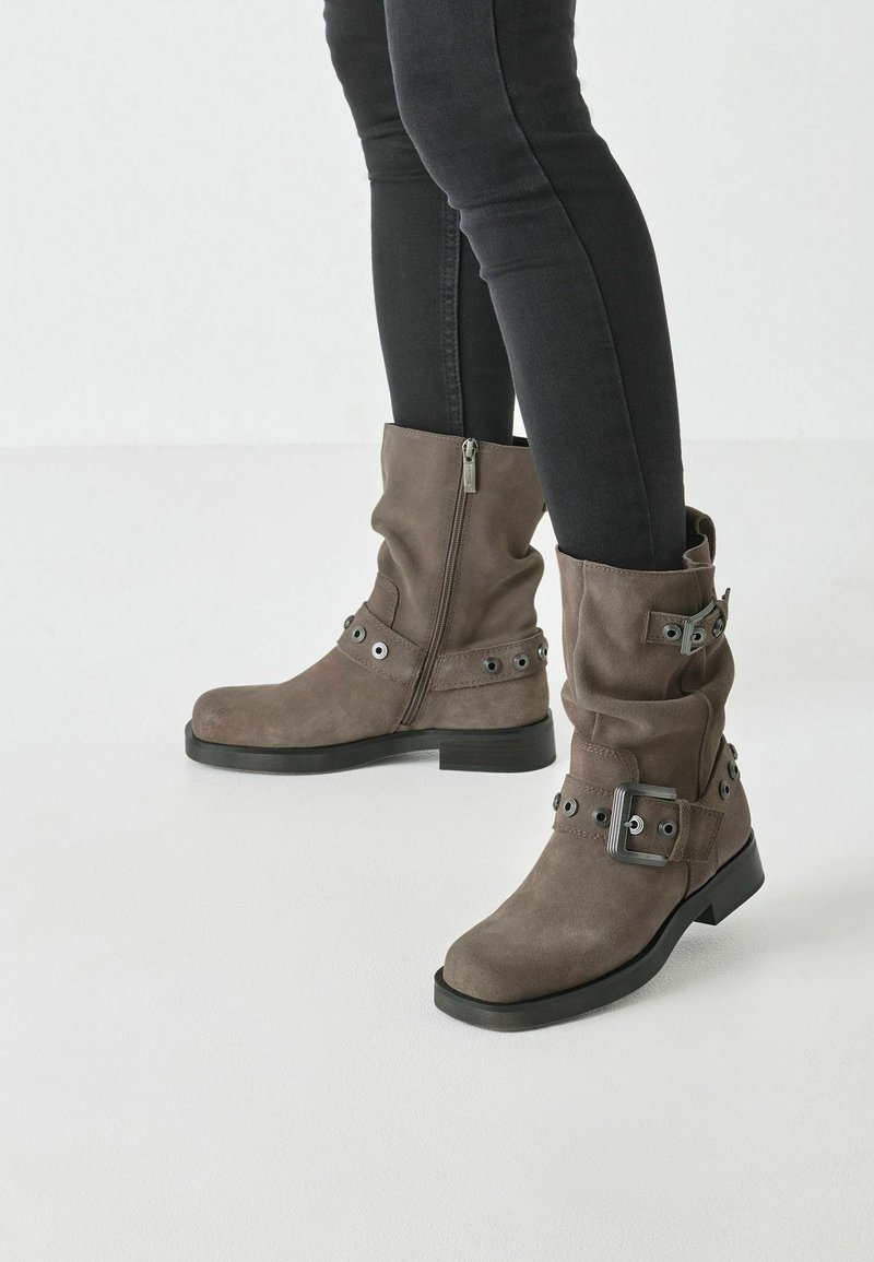Botines de ante gris con cremalleras laterales, hebillas y acentos metálicos; suelas de goma gruesa; diseño arrugado; acabado texturizado.