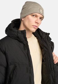 Sort pufferjakke med høj krave og hætte, med lynlås- og velcro-lukninger. Lysegrå ribbet hue med et logo-patch.