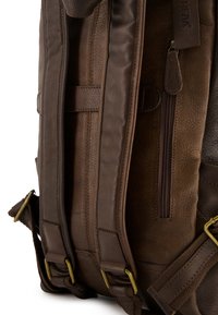 Brązowy plecak ze skóry z teksturowanym materiałem, regulowanymi, wyściełanymi ramiączkami, zamykaną kieszonką oraz mosiężnymi akcentami zapewniającymi trwałość.