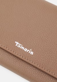 Brown textured faux leather wallet featuring a white Tamaris logo, finely stitched edges, and a smooth finish.