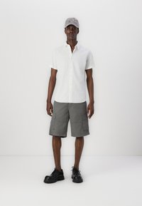 White short-sleeve button-up shirt, gray cargo shorts with pockets, and black shoes. Gray cap with embroidered detailing.
