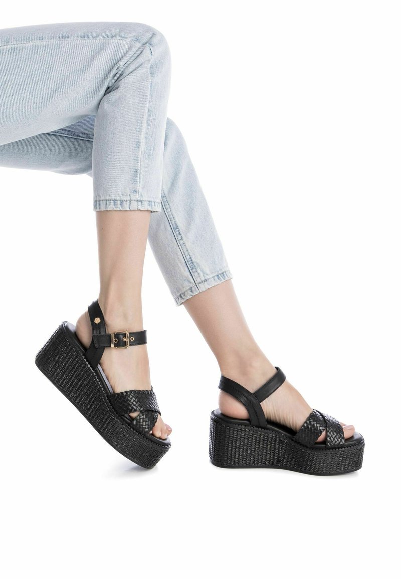 Sandalias de plataforma negras con textura trenzada en las correas, hebilla en el tobillo y una suela gruesa y estriada. Altura casual con ajuste seguro.