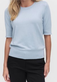 Světlomodrý krátký pletený svetr s kulatým výstřihem a žebrovaným lemem, v kombinaci s černými kalhotami. Hladká textura, volný střih.