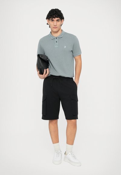 Γκρι βαμβακερό πόλο πουκάμισο με πλακέτα δύο κουμπιών, σε συνδυασμό με μαύρα cargo σορτς με πλαϊνές τσέπες και λευκά αθλητικά παπούτσια με μπεζ λεπτομέρειες.