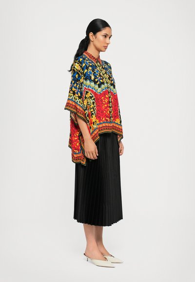 Colorful patterned poncho with a floral design in red, blue, and yellow, paired with a black pleated skirt and white slip-on shoes.
