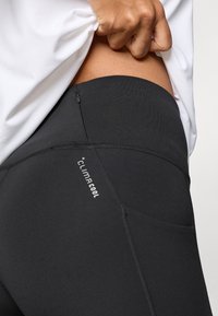 Schwarze Leggings mit hohem Bund und glatter Textur, mit einer kleinen Reißverschlusstasche und "ClimaCool"-Markierung an der Seitennaht.