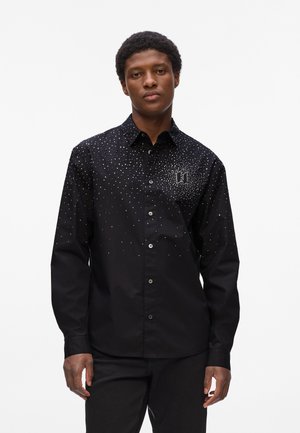 Black button-up shirt with a fitted design, featuring metallic studs arranged in a gradient pattern, and a small logo on the chest area.