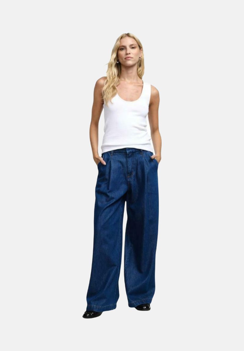 Top bianco senza maniche abbinato a jeans in denim blu a gamba larga. I jeans sono a vita alta con una vestibilità rilassata e tasche laterali. Texture liscia.