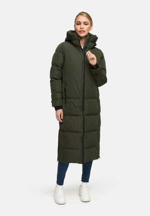 Cappotto lungo imbottito di colore verde scuro con cappuccio, zip frontale completa, tasche laterali e design trapuntato, abbinato a jeans blu e sneakers bianche.