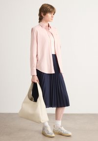 Camicia a maniche lunghe rosa chiaro, gonna plissettata blu navy, borsa hobo beige e sneakers argentate con accenti gialli; texture liscia e materiali morbidi.