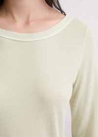 Lys grønn langermet topp med en bred, ribbet hals. Stoffet ser mykt ut med en glatt tekstur og en tettsittende silhuett.