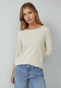 Light beige long-sleeve top with a scoop neckline, made of a soft fabric, paired with blue denim jeans. Simple design, minimal detailing.