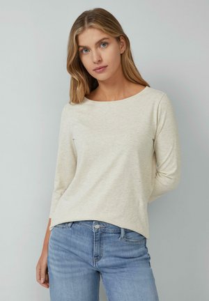 Haut beige clair à manches longues avec un col rond, fabriqué en tissu doux, associé à un jean en denim bleu. Design simple, détails minimaux.