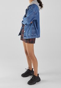 Spijkerjack met een grijze hoodie eronder, gecombineerd met een geruite rok. Zwarte chunky sneakers maken de look af.