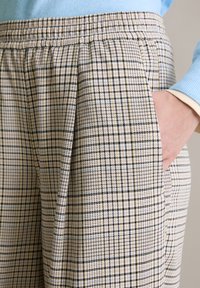 Geruite broek met een patroon in crème en zwart, elastische tailleband, zijzakken en een getextureerde stof. Voorzien van subtiele gele en blauwe accenten.