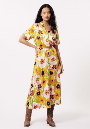Bloemige, knoop-om dress in roze, groen, oranje en blauwe tinten. Kenmerken korte mouwen, een tailleband en een lange, vloeiende rok. Bruine laarzen.