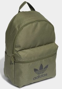 Zeleni platneni ruksak s zaobljenim vrhom, prednjim džepom na zip i crnim Adidas logotipom. Podesive prugaste naramenice za nošenje.