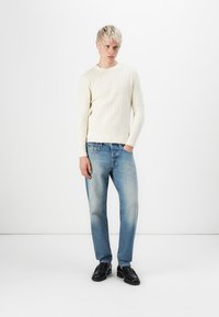Cream knitted sweater with a textured wave pattern, paired with light blue straight-leg jeans and black lace-up shoes.