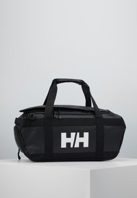 Bolsa de deporte negra, impermeable, con asas dobles en la parte superior y un logo blanco. Cuenta con un cierre con cremallera y un diseño elegante y angular.