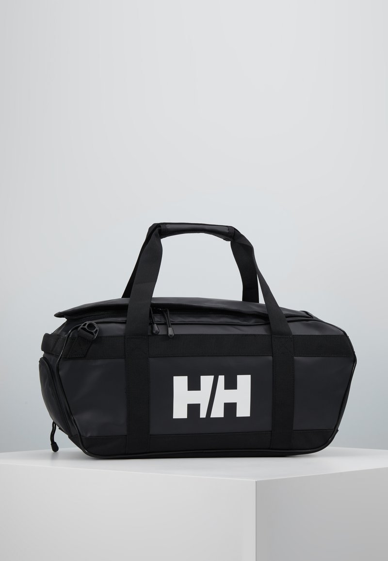 Bolsa de deporte negra, impermeable, con asas dobles en la parte superior y un logo blanco. Cuenta con un cierre con cremallera y un diseño elegante y angular.