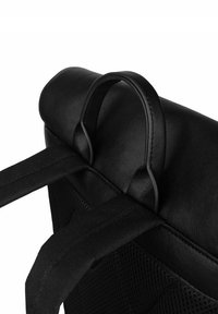 Detail černé kožené tašky obsahující kulatou rukojeť a tkané látkové popruhy, s texturovaným tělem a síťovaným akcentem pro prodyšnost.