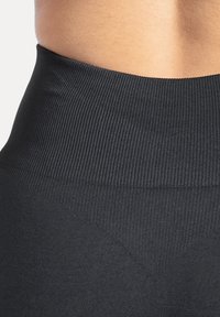 Leggings neri a vita alta realizzati in tessuto elasticizzato, con una fascia in vita a coste e una texture liscia con un sottile motivo a forma di V.