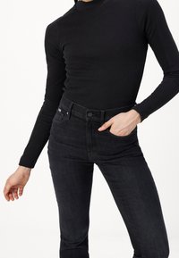 Top negro de manga larga con textura acanalada, combinado con vaqueros oscuros. Los vaqueros tienen un diseño ajustado con bolsillos delanteros y cierre de botón.