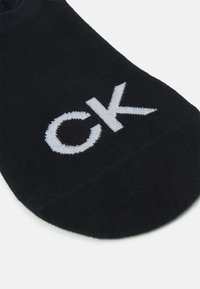 Calcetín negro hasta el tobillo, hecho de una tela suave con una textura lisa, que presenta un logo "CK" bordado en el costado en color blanco.