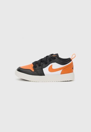 Baskets basses avec des panneaux noirs, orange et blancs, logo Nike orange, lacets noirs et semelle blanche sur un fond neutre.