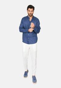 Camicia in lino blu con bottoni, pantaloni in lino bianchi e scarpe in suede blu. La camicia ha un colletto e maniche lunghe.