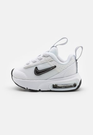 Zapatilla pequeña blanca de Nike con logo negro Swoosh, parte superior de malla, amortiguación de aire visible en la suela y tiradores en la lengüeta y el talón.