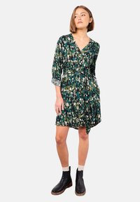 Grünes gemustertes Kleid mit V-Ausschnitt, langen Ärmeln und tailliertem Bund. Es zeigt eine Mischung aus abstrakten Formen in verschiedenen Grüntönen und Weiß.