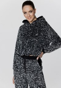 Czarna i srebrna bluzka z cekinami o szerokim kroju, wyposażona w sznurki oraz akcenty guzikowe, zestawiona z pasującymi dresami z cekinami.