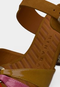 Πέδιλο με λουράκια και ψηλό τακούνι σε κίτρινο, ροζ και καφέ χρώμα. Διαθέτει λείο δερμάτινο δερματίνη και υφασμένες εξωτερικές σόλες. Περιλαμβάνει ασημί μεταλλικά στοιχεία.