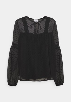 Sort gennemsigtig bluse med et tekstureret polkadot mønster, rund hals og bånddetalje, med blonde accenter og puffede ærmer.