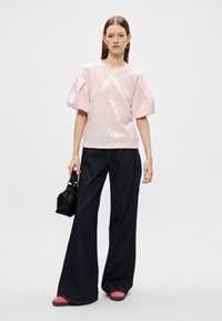 Heledate roosa sädeleva topiga, lühikeste puhviga varrukatega, koos tumedate siniste laia säärega teksade ja roosa aktsendiga jalatsitega. Lisavarustusena on väikse musta koti kaasamine.