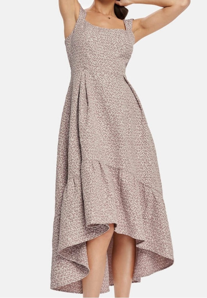 Femme portant une robe sans manches asymétrique avec un motif abstrait subtil, posant avec une main derrière la tête et l’autre levée.