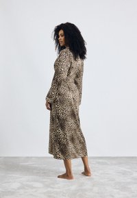 Robe à imprimé animal en tan et noir, à manches longues, mi-longue avec une coupe décontractée. Tissu doux qui tombe harmonieusement, avec une taille ceinturée.