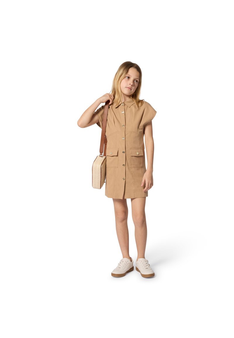 Κοντό φόρεμα με κοντά μανίκια, μπροστινές τσέπες, κλείσιμο με κουμπιά και γιακά. Συνδυασμένο με μικρή μπεζ τσάντα και λευκά αθλητικά παπούτσια.